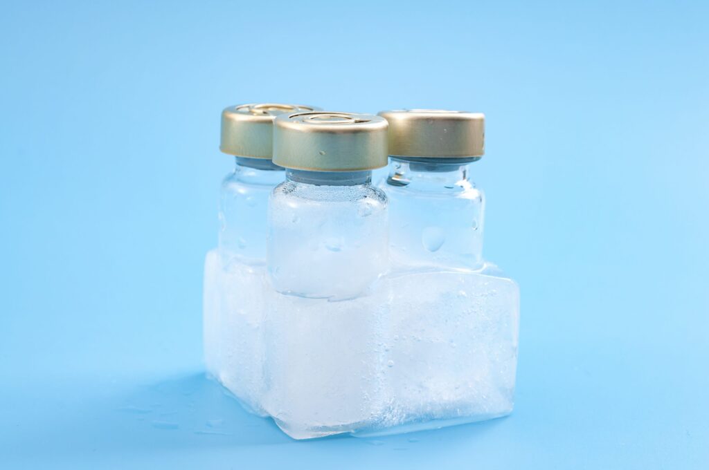 covid treatment and coronavirus vaccination campaign concept with vaccine vials frozen in a chunk of ice isolated on blue background