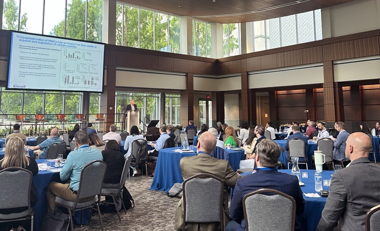 Large conference room with attendees seated at round tables, watching a presentation on biopreservation best practices at The Cell Summit ’25, featuring data slides projected at the front.